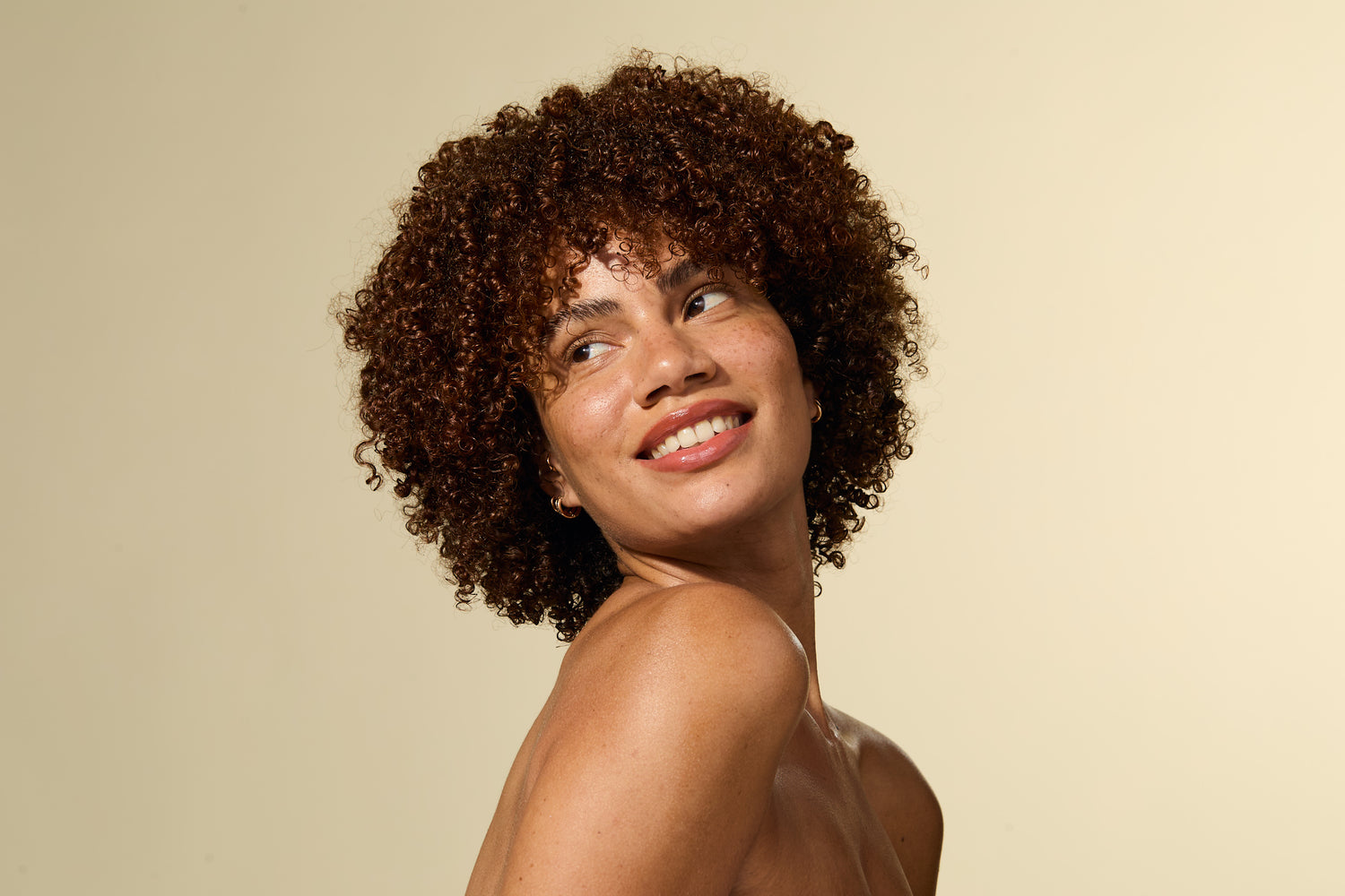 Vrouw met krullend haar glimlacht tegen een beige achtergrond