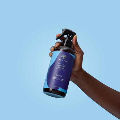 Hand met een fles AS I AM Deodorant Spray tegen een helderblauwe achtergrond