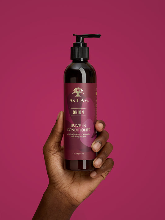 Hand met een fles 'As I Am' Onion Leave-In Conditioner tegen een roze achtergrond