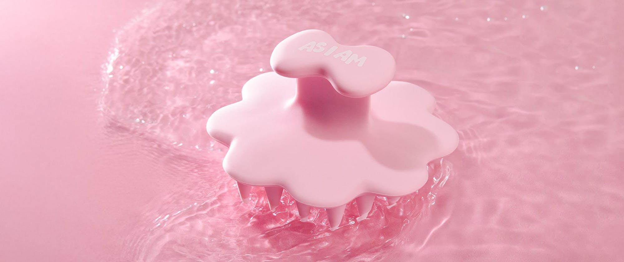 Roze hoofdhuidborstelproduct met waterdruppels op een roze achtergrond