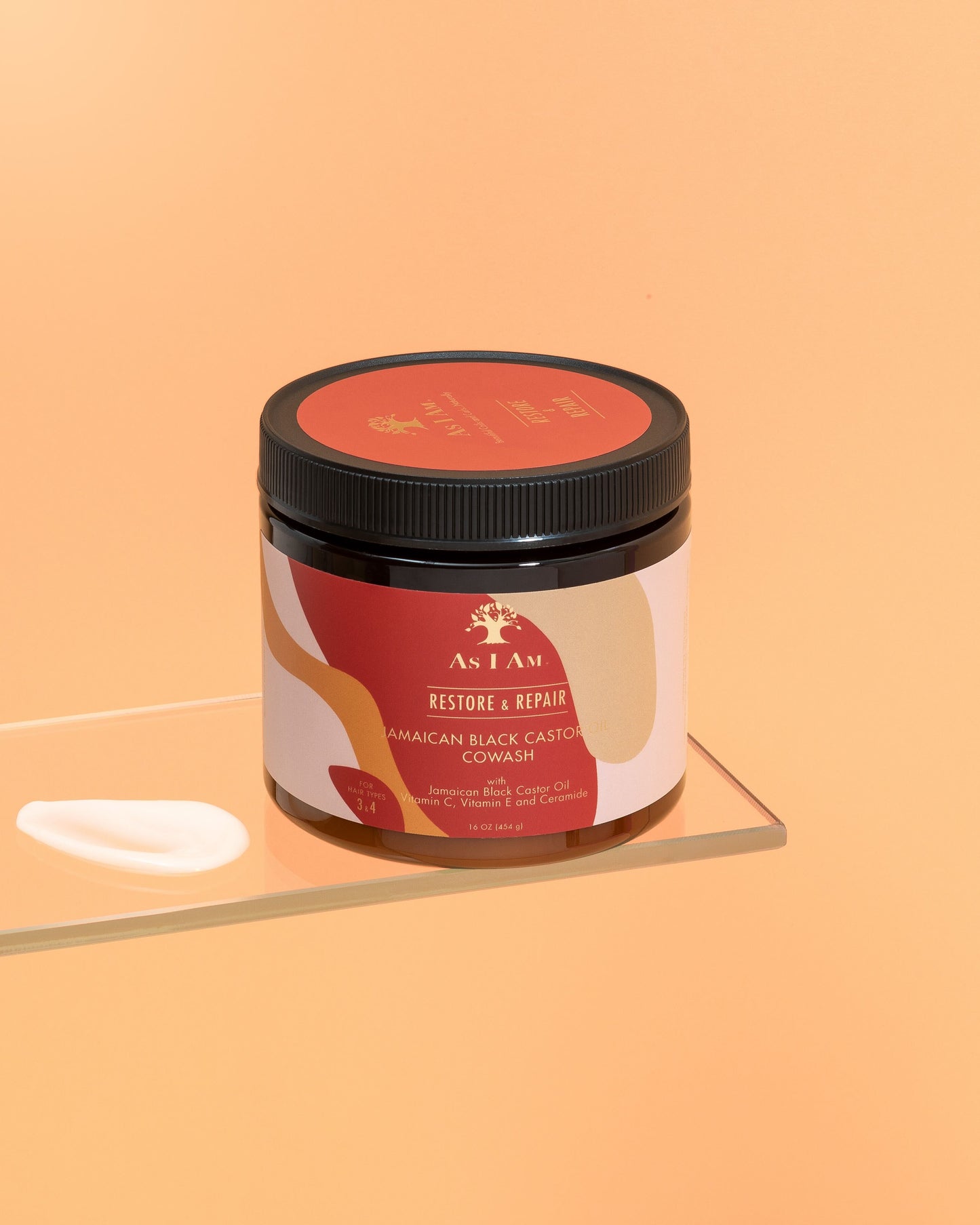 Een container met Jamaicaanse zwarte ricinusolie Cowash met een etiket waarop productdetails staan vermeld, geplaatst op een reflecterend oppervlak met een effen oranje achtergrond.