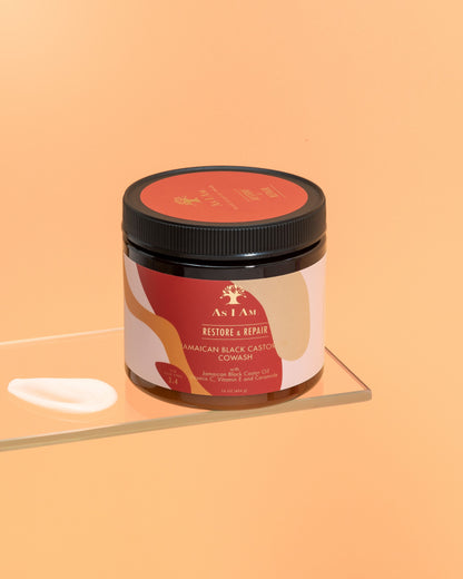 Een container met Jamaicaanse zwarte ricinusolie Cowash met een etiket waarop productdetails staan vermeld, geplaatst op een reflecterend oppervlak met een effen oranje achtergrond.